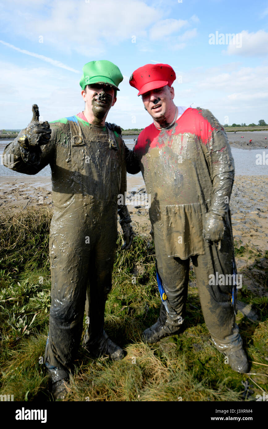 I concorrenti della MAD Maldon Mud Race hanno coperto di fango dalle corse attraverso e attraverso il fiume Blackwater nell'Essex, Regno Unito Foto Stock