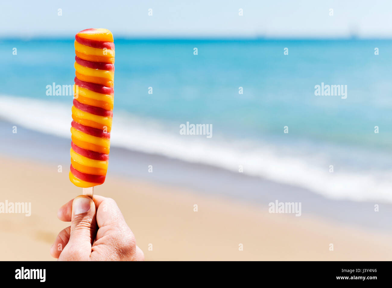 Primo piano di un rinfrescante ghiaccioli nella mano di un giovane uomo caucasico sulla spiaggia con lo spazio negativo sul lato destro Foto Stock