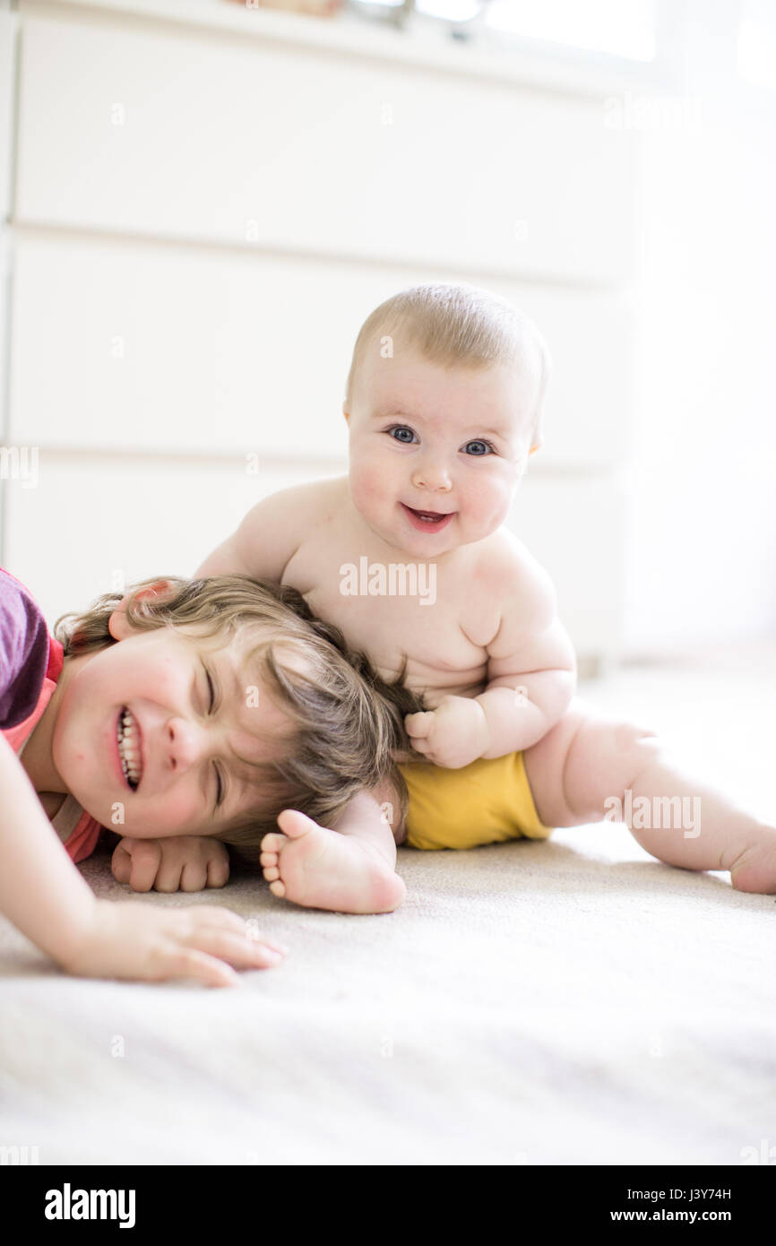 Ritratto di happy Baby girl tirando il grande fratello i capelli sul letto Foto Stock