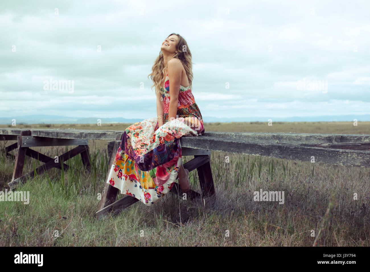 Giovane donna in boho abito maxi seduta sulla sopraelevata passerella in legno in orizzontale Foto Stock