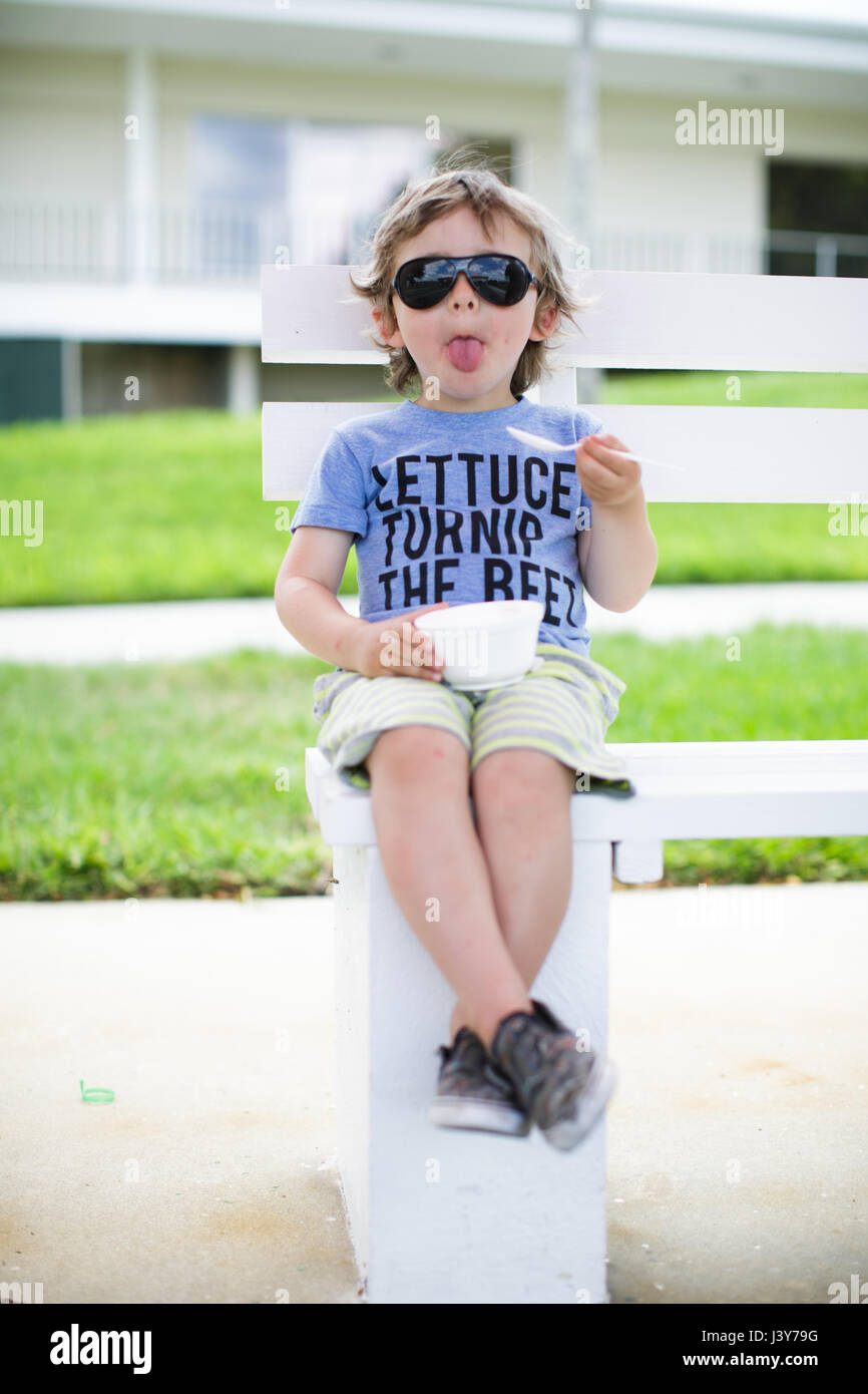 Ritratto di ragazzo seduto sul banco di mangiare la coppa di gelato Foto Stock