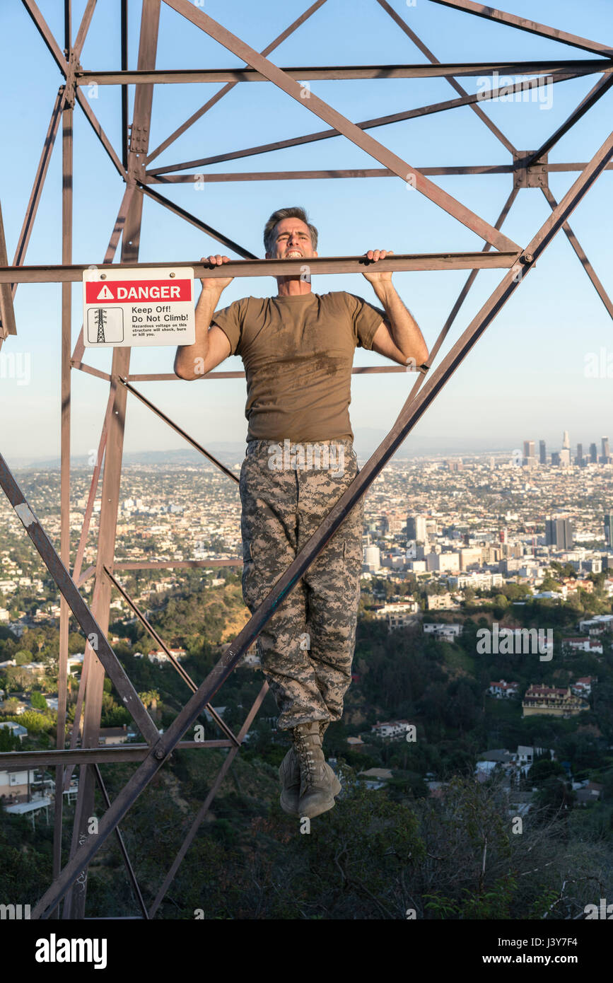 Soldato indossando indumenti di combattimento facendo chin ups sul traliccio di elettricità, Runyon Canyon, Los Angeles, California, Stati Uniti d'America Foto Stock