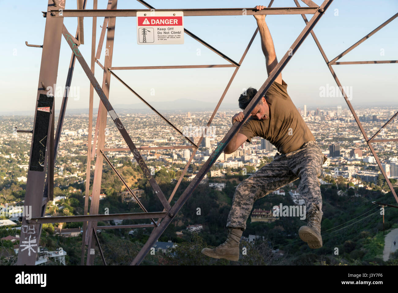 Soldato indossando indumenti di combattimento penzolante dal traliccio di elettricità, Runyon Canyon, Los Angeles, California, Stati Uniti d'America Foto Stock