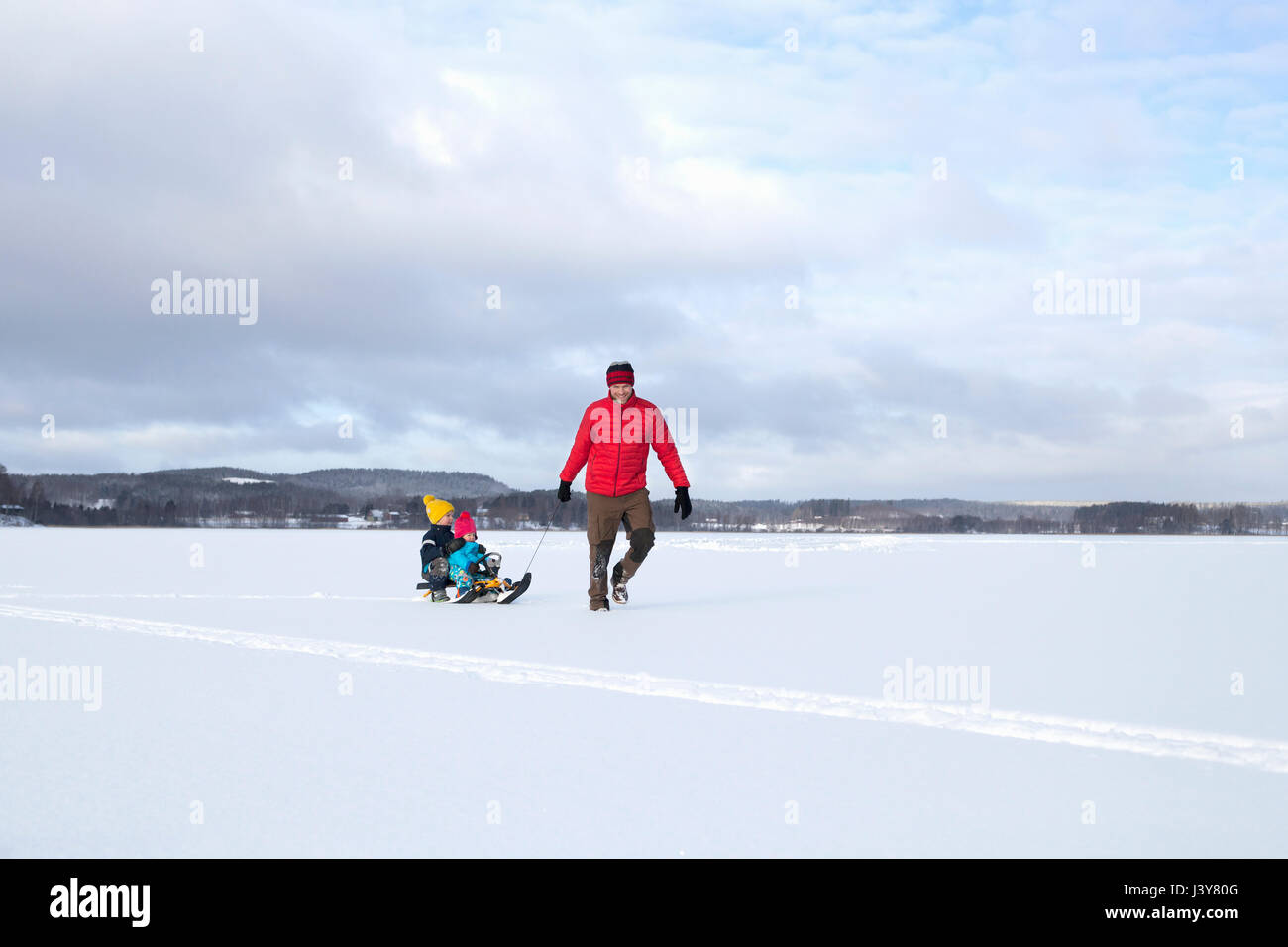 Padre figli di trazione lungo sulla slitta in paesaggi innevati Foto Stock