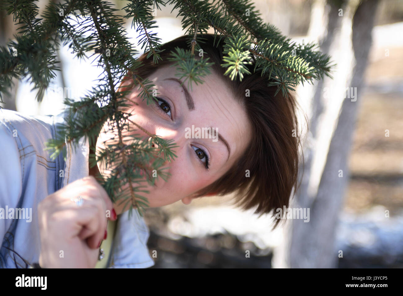 Ritratto di giovane e bella ragazza sotto albero di abete rosso e guardando alla fotocamera Foto Stock