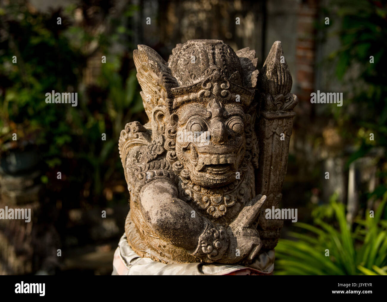 Un antica divinità di pietra con barba e capelli ricci, occhi rotondi, grandi denti e zanne, situato nella foresta tropicale di Bali. Foto Stock