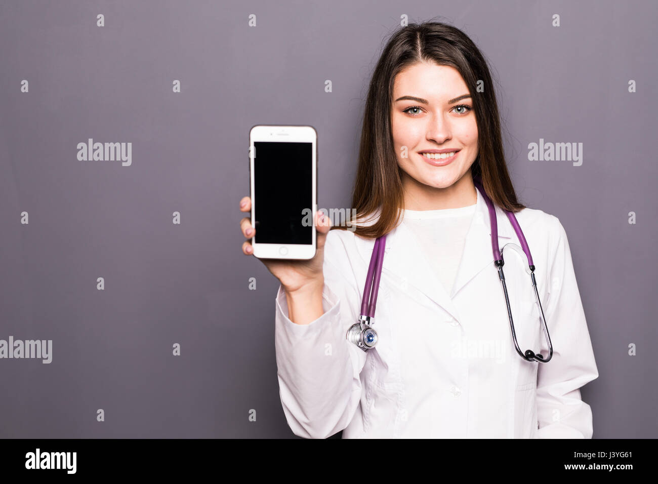 Giovani donne medico mostra telefono mobile contro il grigio Foto Stock