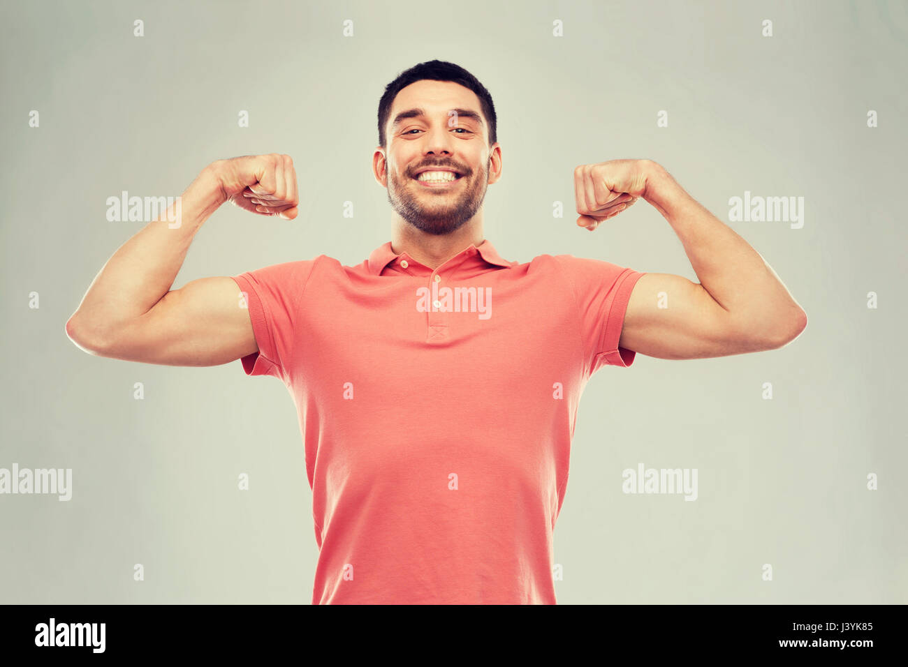 Uomo sorridente mostra bicipite su sfondo grigio Foto Stock