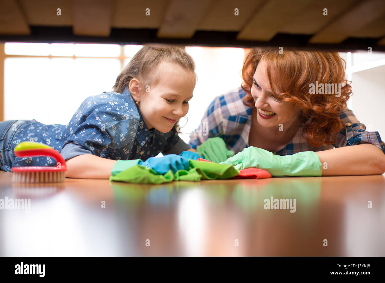 Famiglia sorridente madre e bambino ragazza camera pulita a casa. L'età media di donna e bambino ragazza spazzato il pavimento sotto il letto Foto Stock