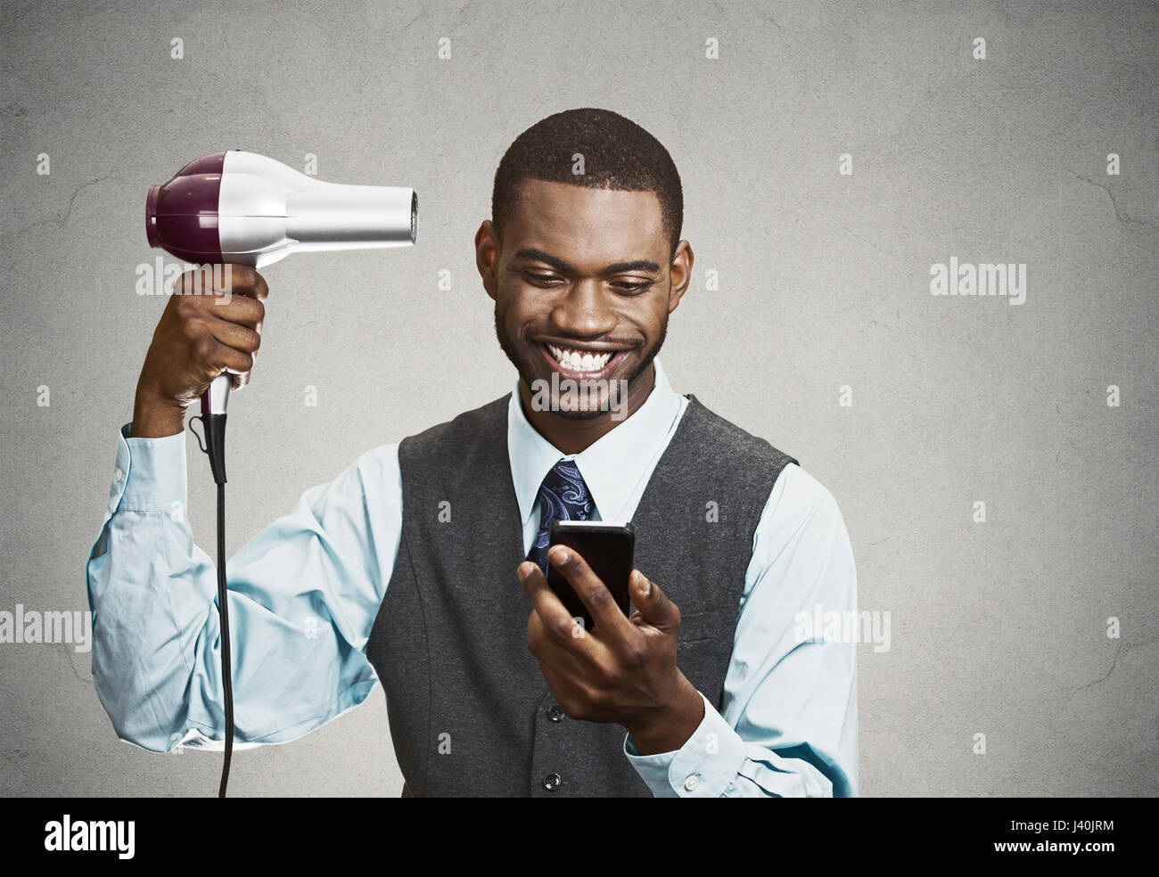 Closeup ritratto felice, sorridente uomo d affari e trattare maker la lettura di buone notizie su smart, telefono cellulare, tenendo asciugacapelli isolato nero lo sfondo grigio. H Foto Stock