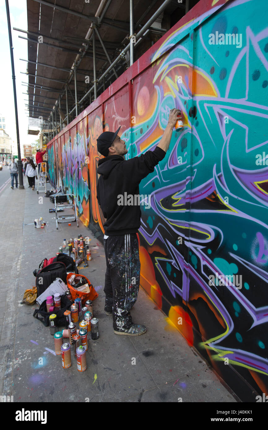 L'artista di strada verniciatura a spruzzo graffiti murale sulla palizzata lungo la Great Eastern Street, Shoreditch, East London, Regno Unito Foto Stock
