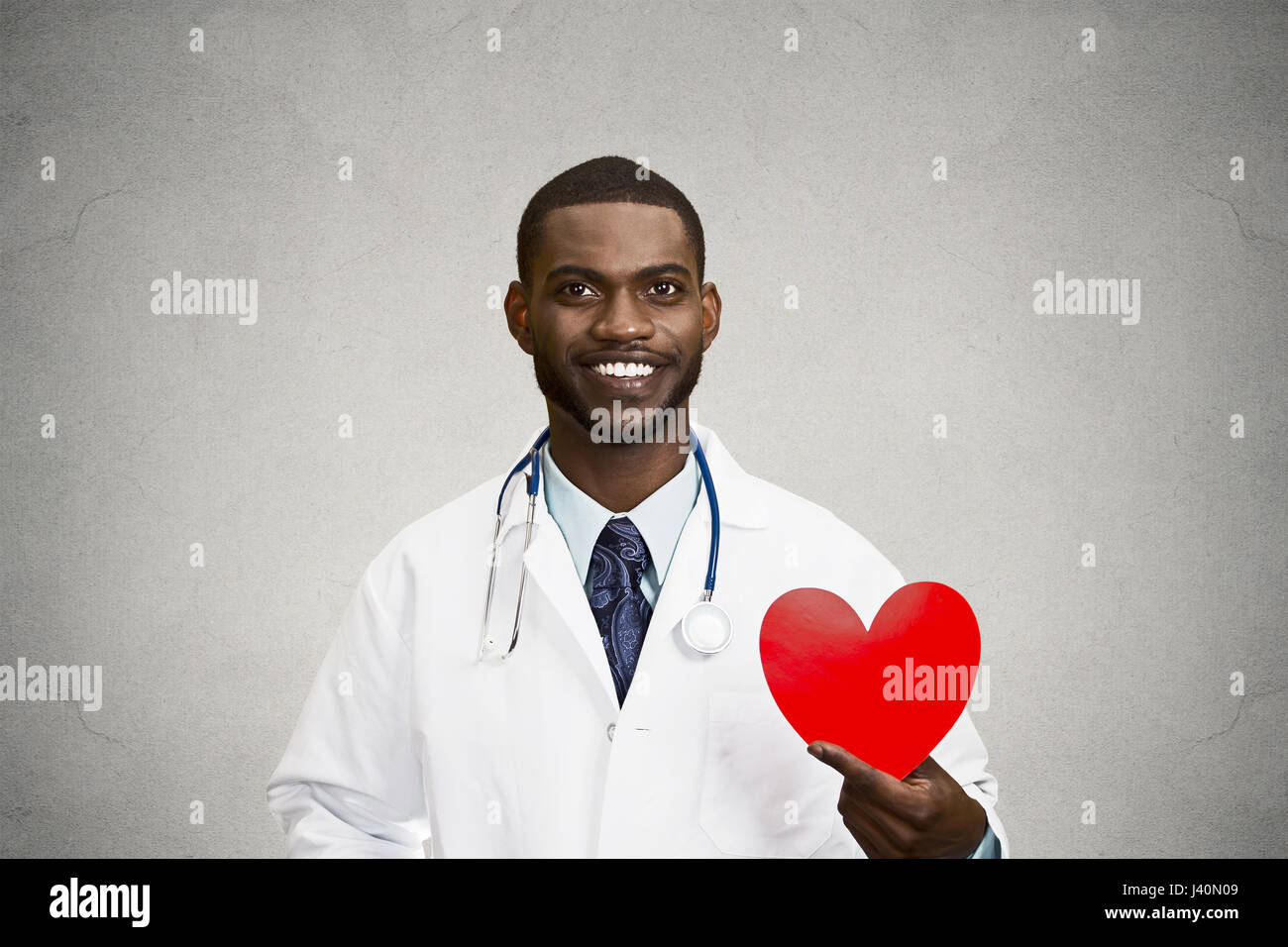 Closeup ritratto felice, maschio sorridente professionista sanitario, l uomo dal medico di famiglia, cardiologo con uno stetoscopio holding cuore rosso, isolato nero, gre Foto Stock