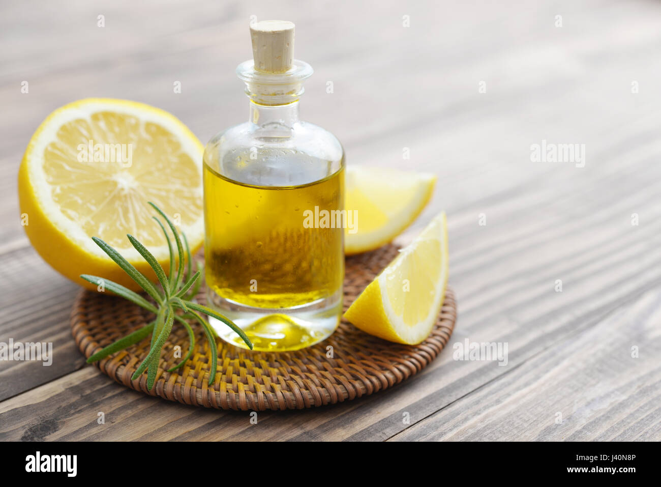 Olio di limone in una bottiglia di vetro con limoni freschi su sfondo di legno Foto Stock