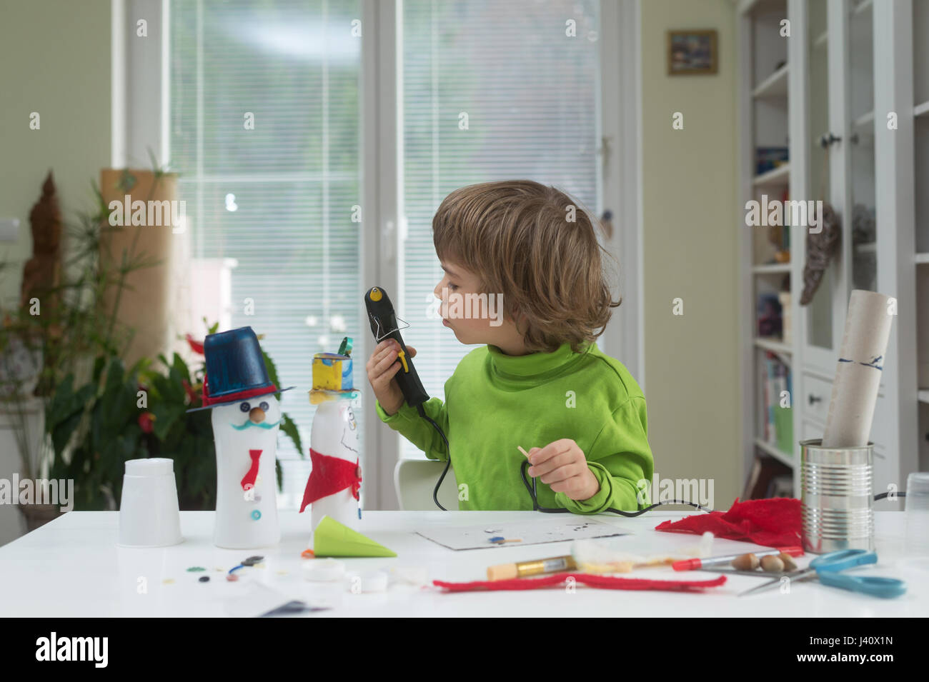 Little Boy essere creativi rendendo in casa fai-da-te giocattoli fuori della bottiglia di yogurt e carta tramite pistola per colla a caldo. Il supporto di creatività, di apprendimento Foto Stock