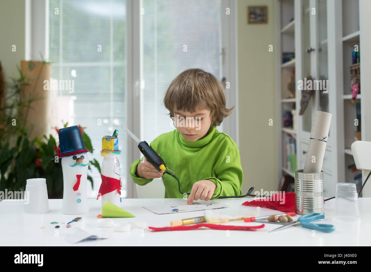 Little Boy essere creativi rendendo in casa fai-da-te giocattoli fuori della bottiglia di yogurt e carta tramite pistola per colla a caldo. Il supporto di creatività, di apprendimento Foto Stock
