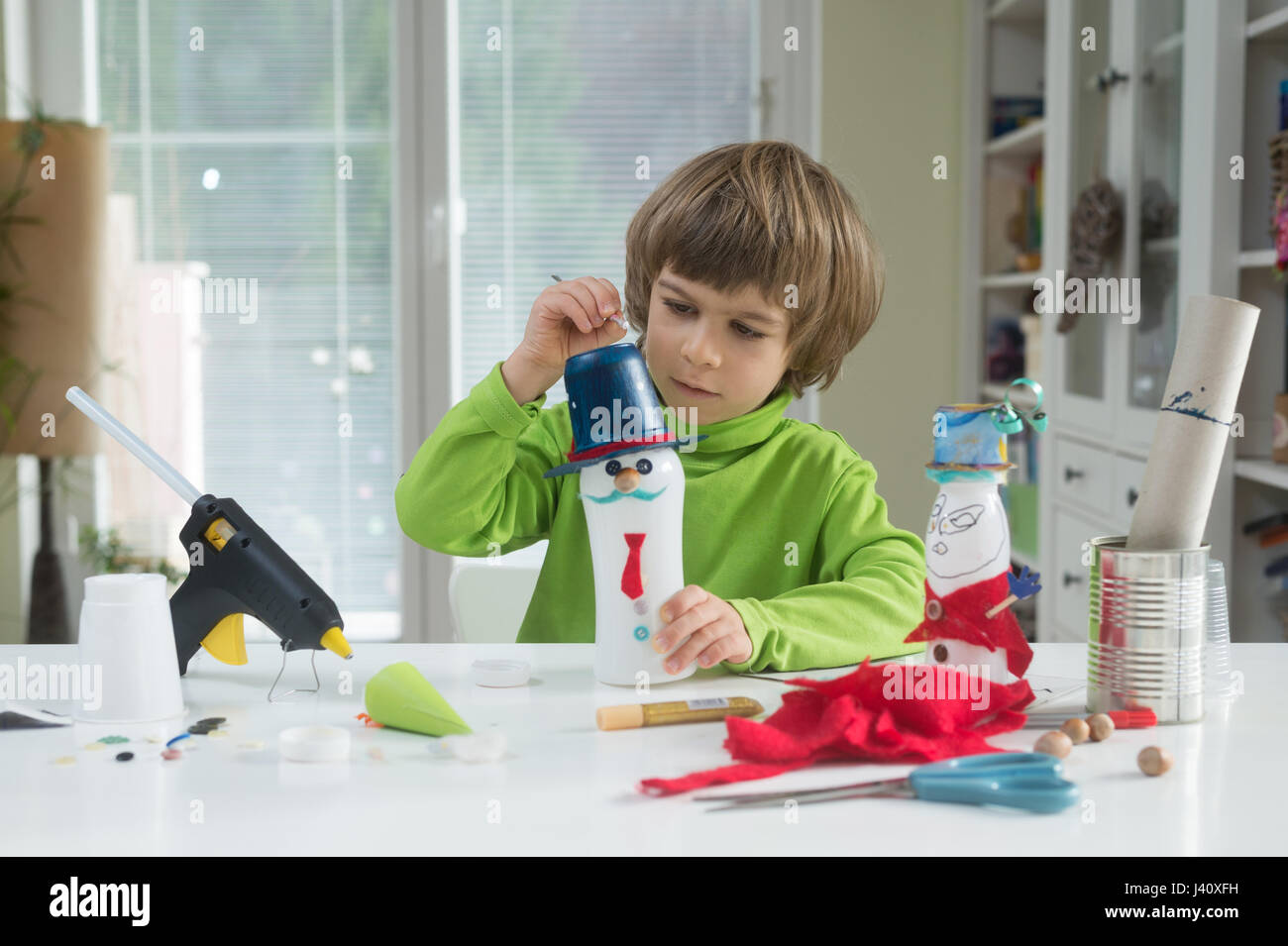 Little Boy essere creativi rendendo in casa fai-da-te giocattoli fuori della bottiglia di yogurt e carta tramite pistola per colla a caldo. sostenere la creatività, l'apprendimento. Foto Stock
