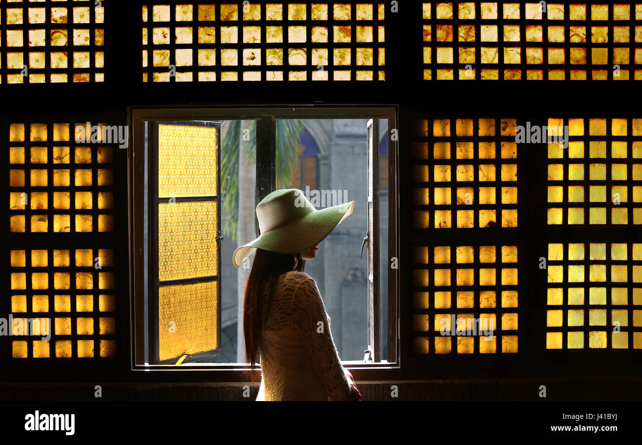 Donna in piedi dalla finestra di capiz all'interno di San Agustin chiesa, Intramuros, Manila, Filippine, Asia Foto Stock