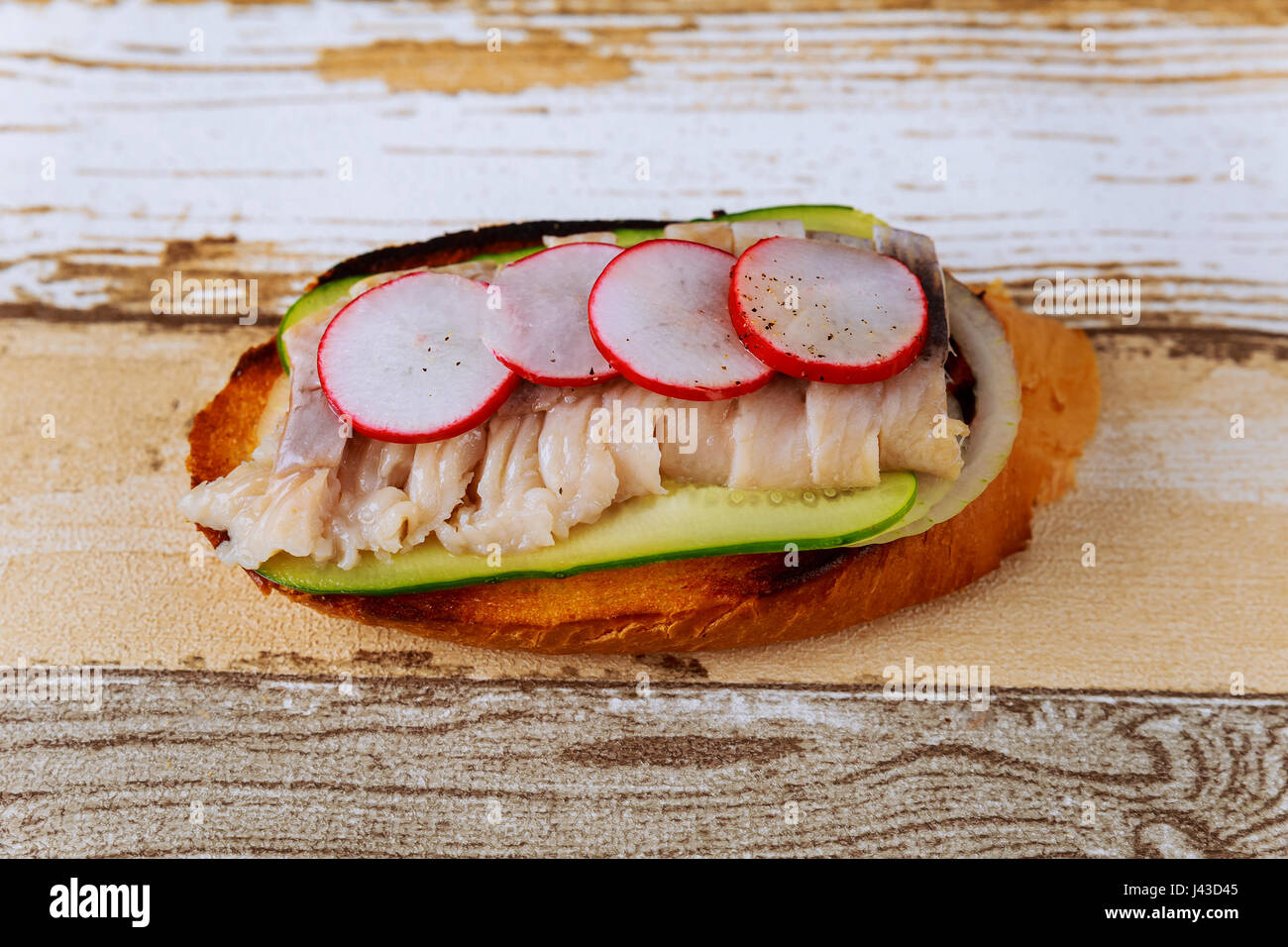 Panini con le aringhe, cetrioli sottaceto, il ravanello e la cipolla sul tagliere Foto Stock