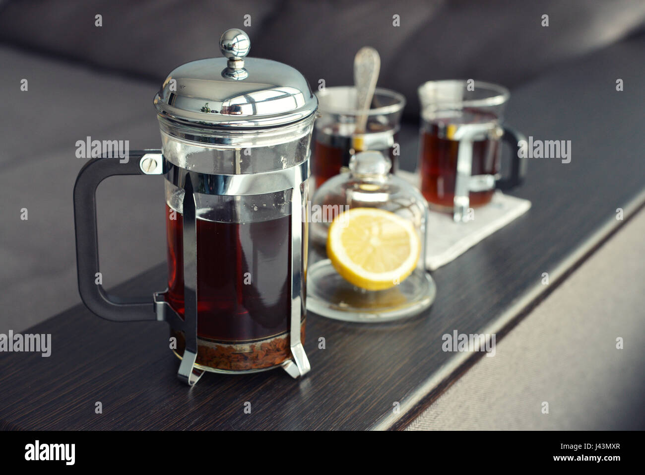 Tazze di tè con french press e limone sul divano nel soggiorno closeup. Foto Stock