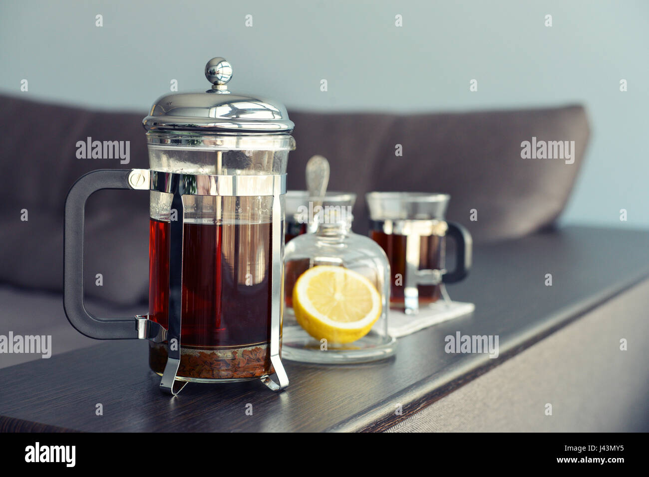 Tazze di tè con french press e limone sul divano nel soggiorno closeup. Foto Stock