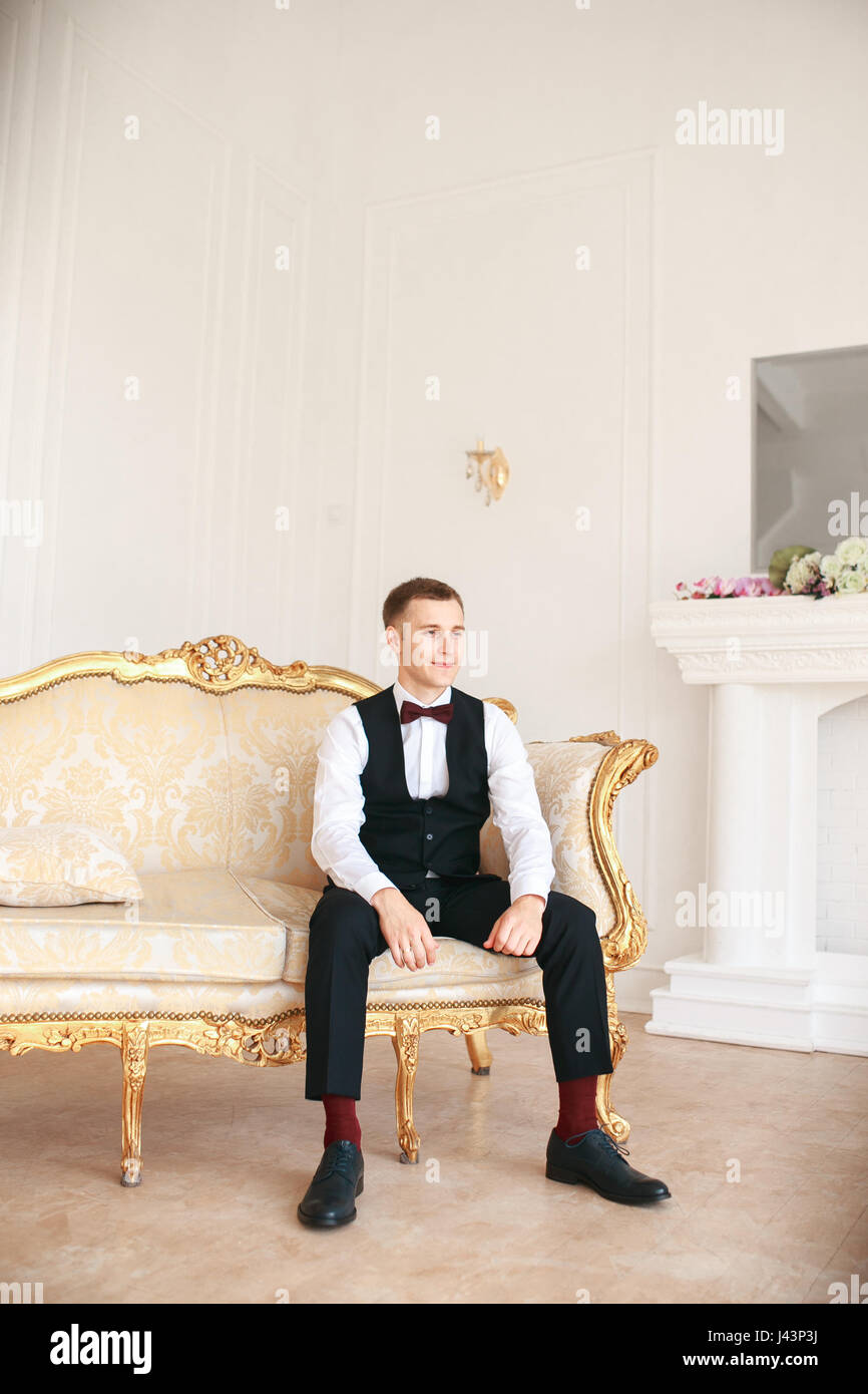 Lo sposo seduto sul divano in attesa che la sposa per il suo giorno di nozze. ad un matrimonio tuxedo sorridente e in attesa di sposa.uomo elegante in costume nero e b Foto Stock