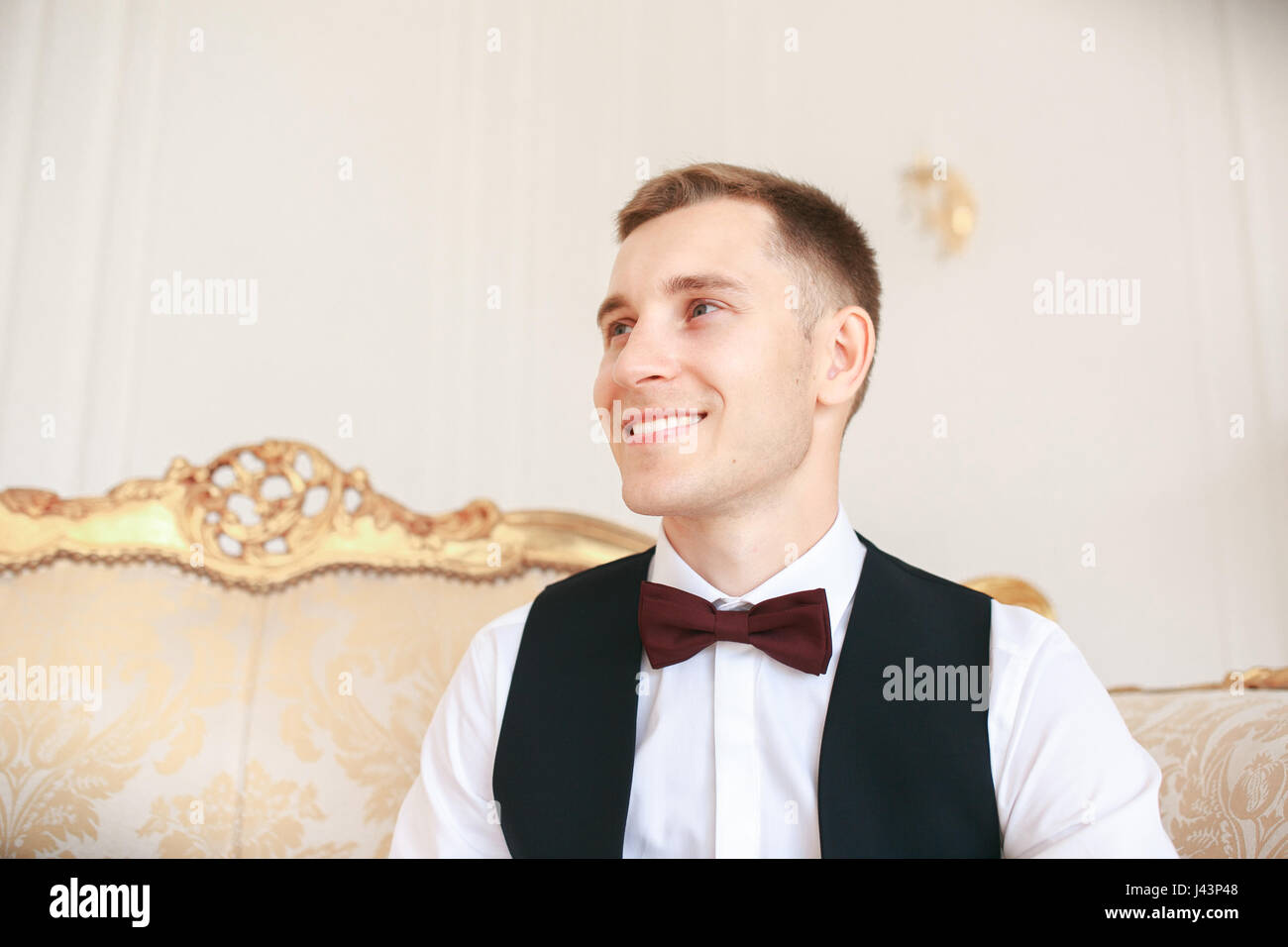 Lo sposo seduto sul divano in attesa che la sposa per il suo giorno di nozze. ad un matrimonio tuxedo sorridente e in attesa di sposa.uomo elegante in costume nero e b Foto Stock