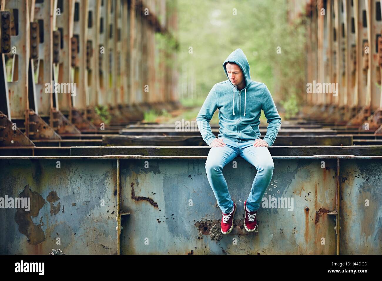 Triste uomo seduto sull'abbandonato ponte arrugginito. Concetto di tristezza e di solitudine e di più. Foto Stock