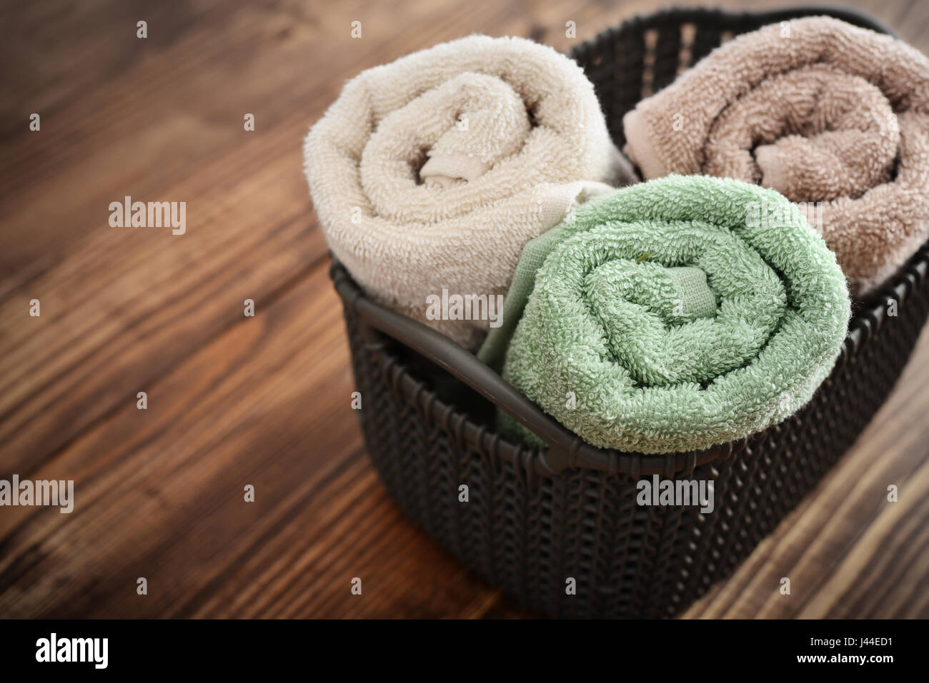 Asciugamani da bagno di colori diversi nel cesto in vimini su sfondo di legno Foto Stock