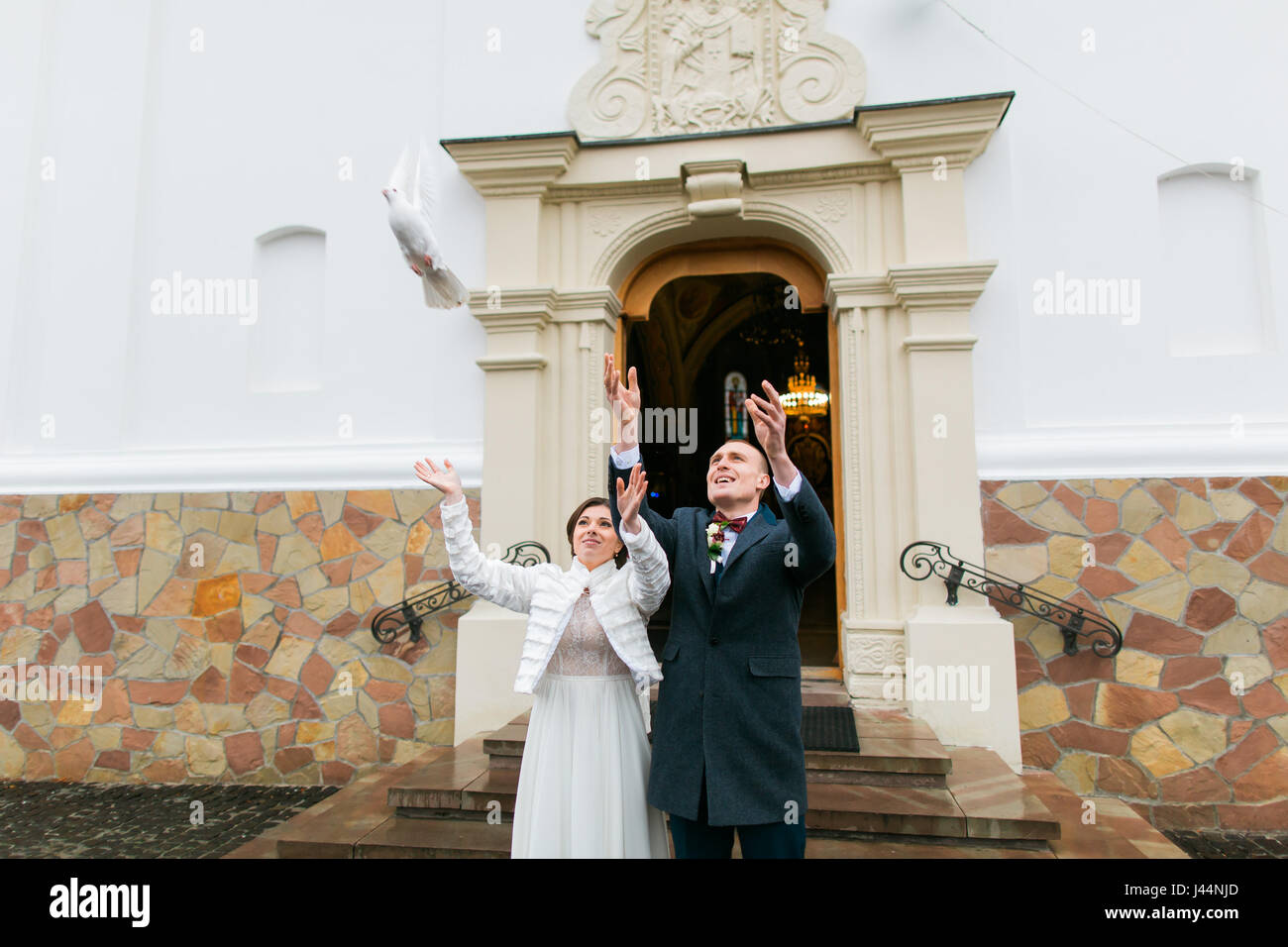 Sposa giovane rilasciando colombe bianche quando si lascia la chiesa dopo la loro cerimonia di nozze Foto Stock