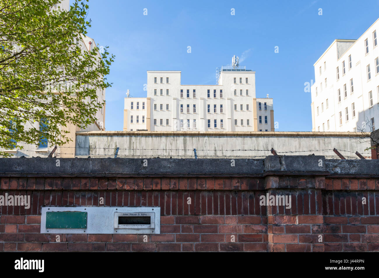 Alcuni dei vecchi 1930 John Player degli edifici adibiti a magazzino dietro un muro di mattoni con letterbox che mostra il nome dell'azienda, Nottingham, Inghilterra, Regno Unito Foto Stock