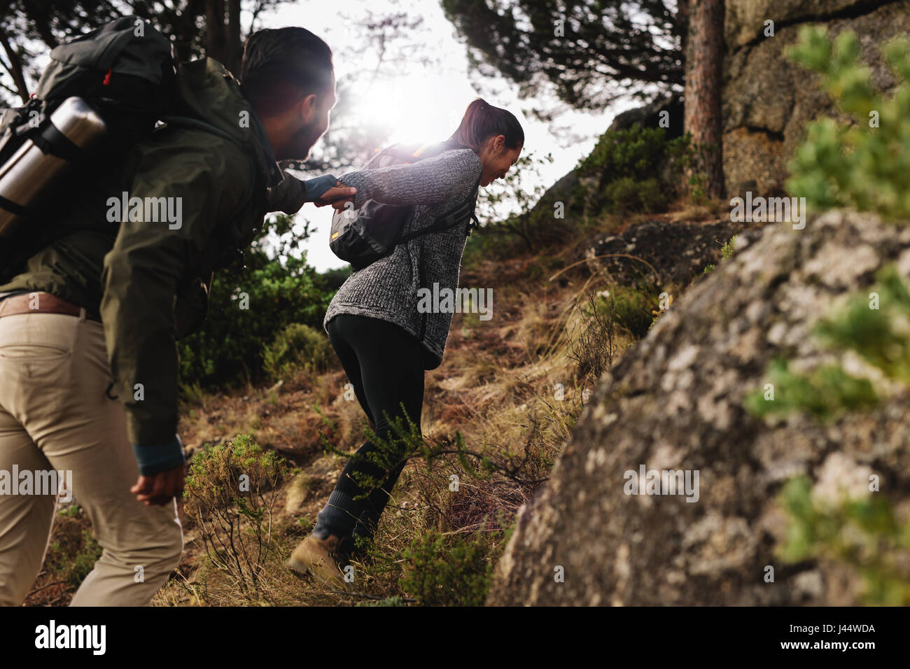 Escursionista femminile aiutando il suo ragazzo in salita in campagna. Coppia giovane escursioni in montagna. Foto Stock