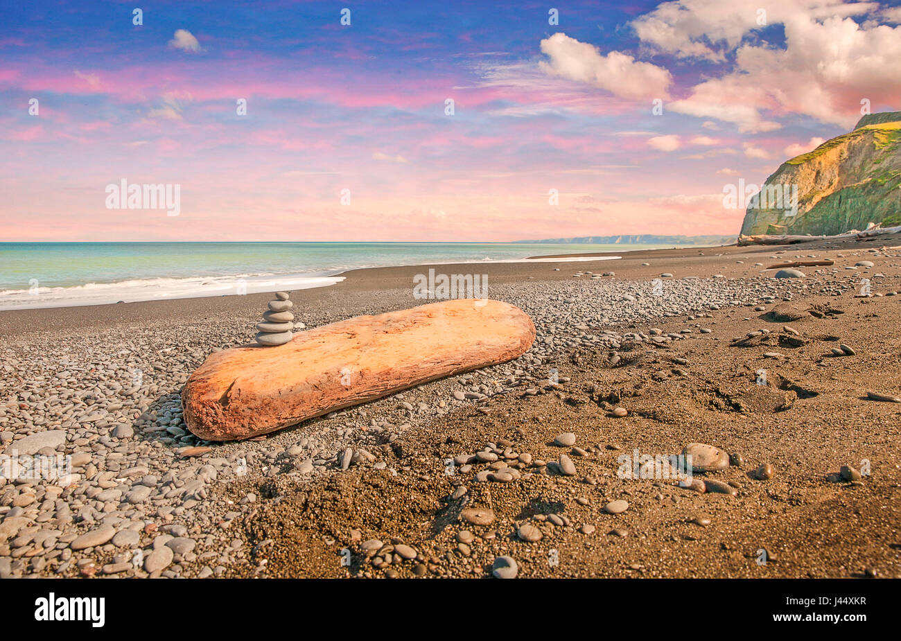 Un mucchio di pietre su un grande pezzo di driftwood lavato fino su una spiaggia in Nuova Zelanda. Foto Stock