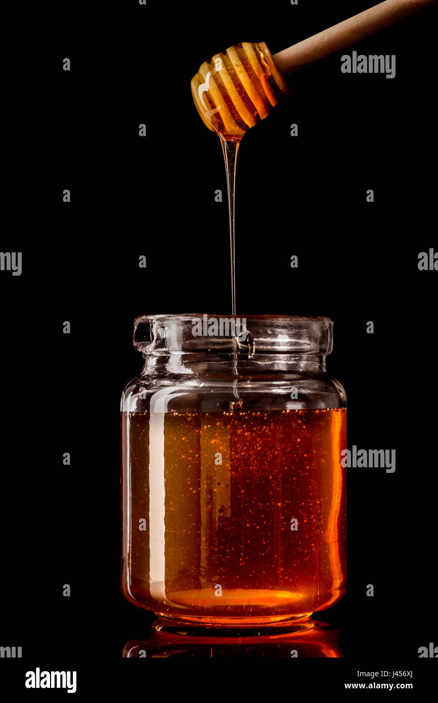 Cucchiaia di miele Il miele di gocciolamento in un barattolo di vetro Foto Stock