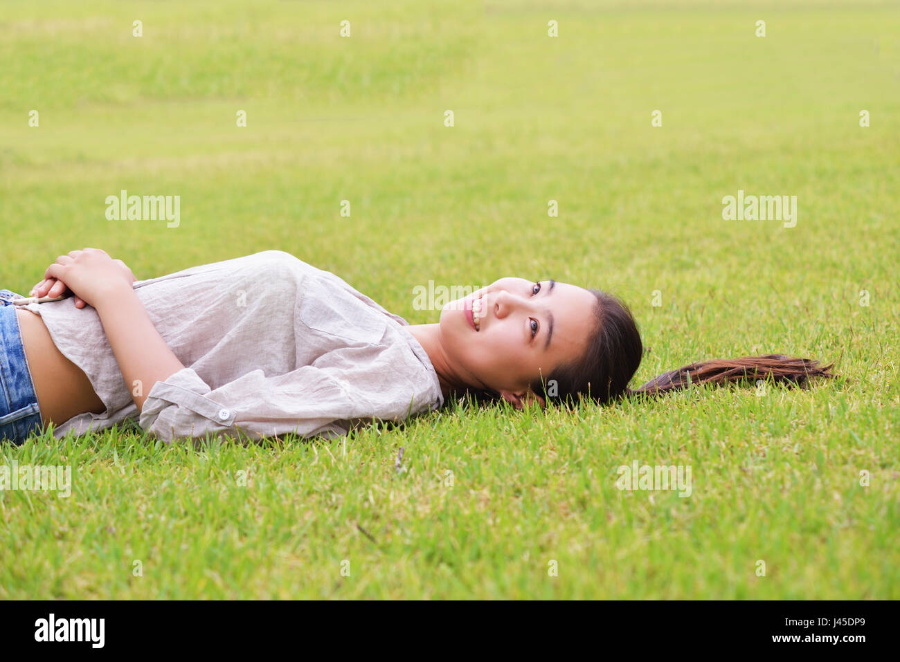 Felice ragazza asiatica giacente in erba Foto Stock