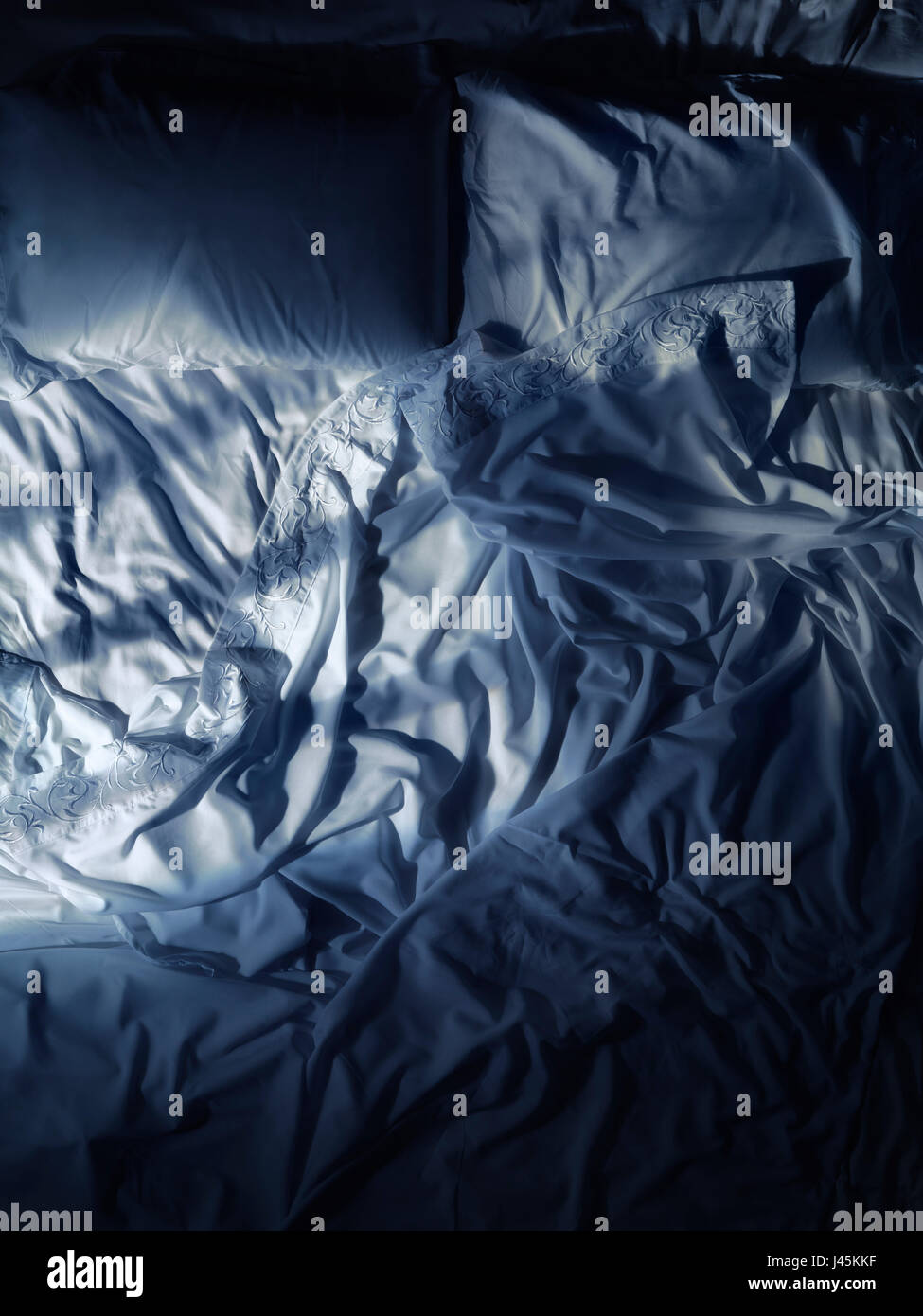 Disfatto letto vuoto, bianco lenzuola poco illuminata dalla luna di notte Foto Stock