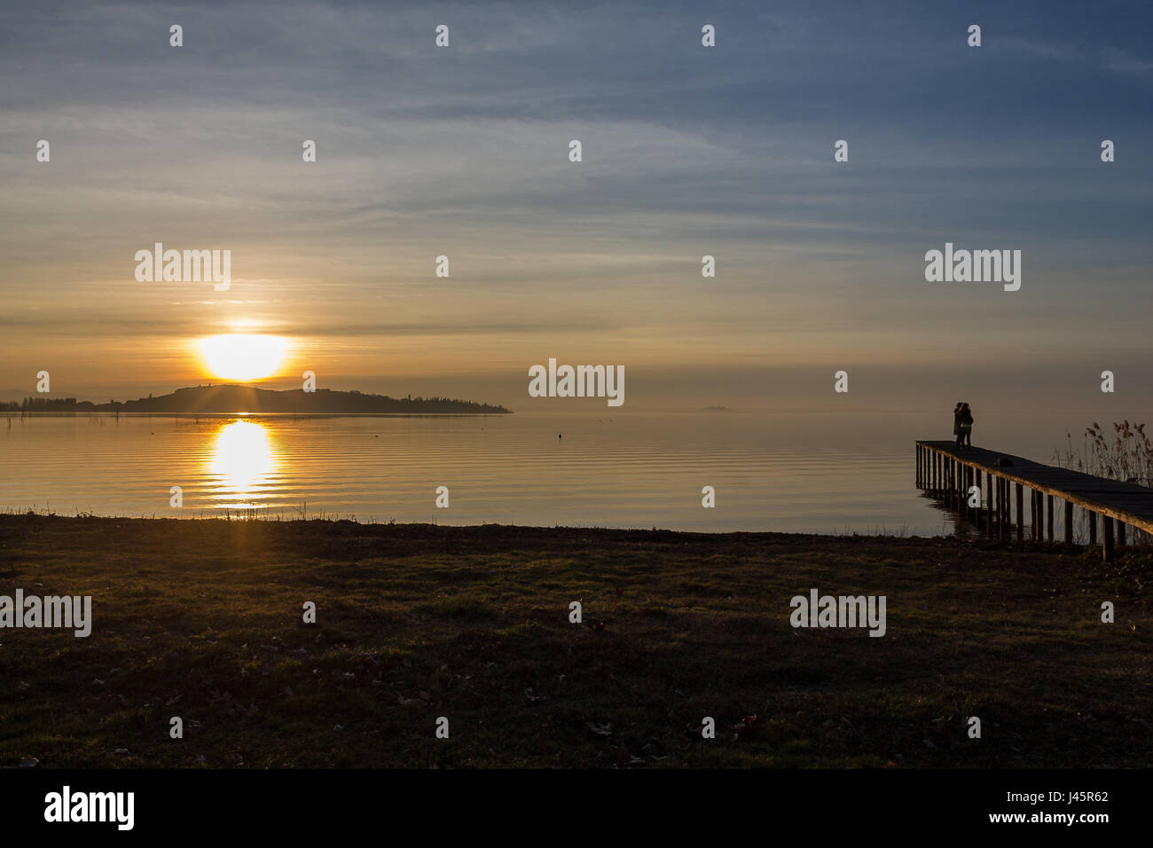 Un giovane su un molo sul lago durante il tramonto Foto Stock