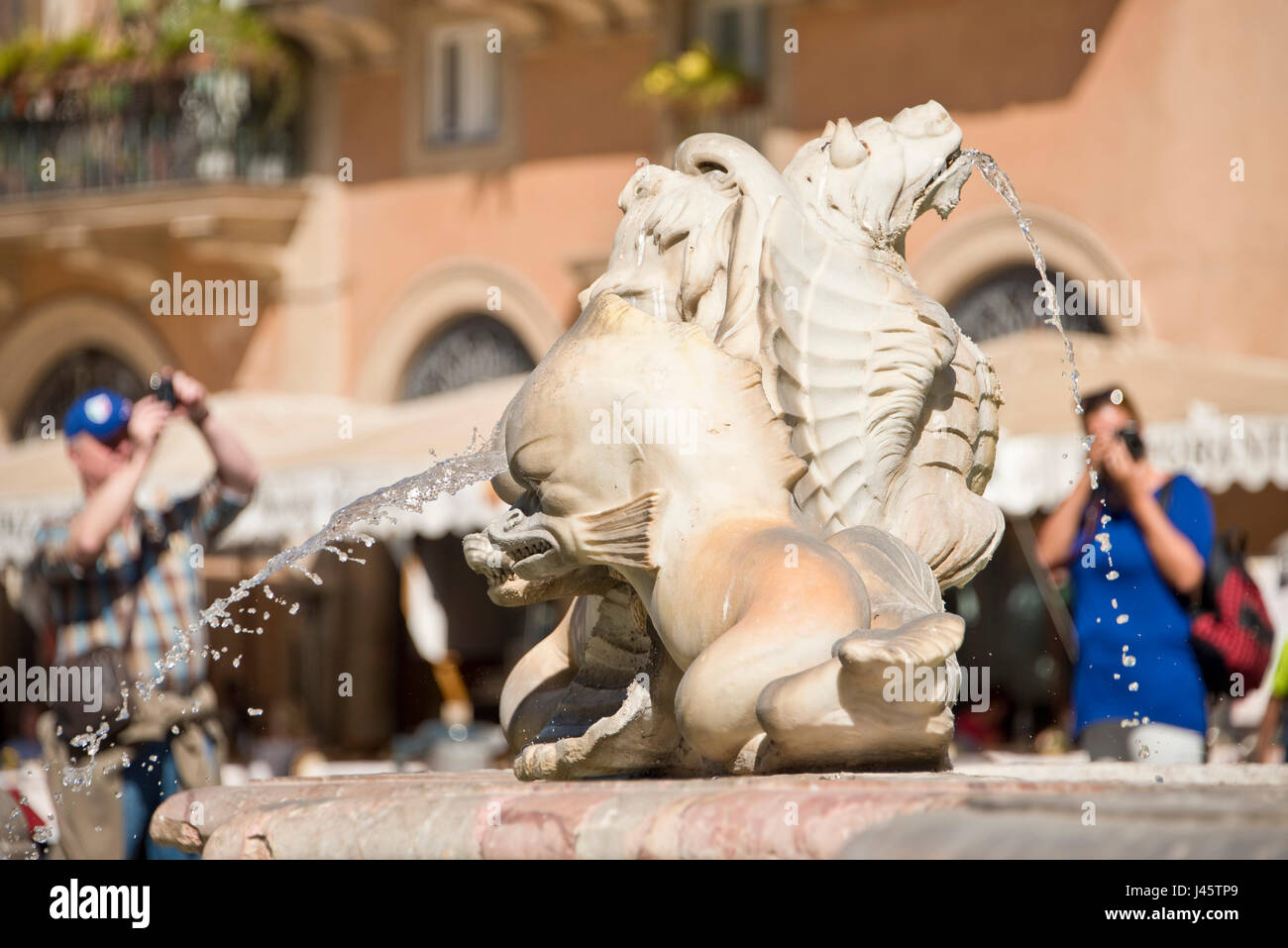 Una chiusura su la Fontana del Moro o la Fontana del Moro in Piazza Navona con 2 fuori fuoco persone turisti visitatori scattano fotografie in background. Foto Stock