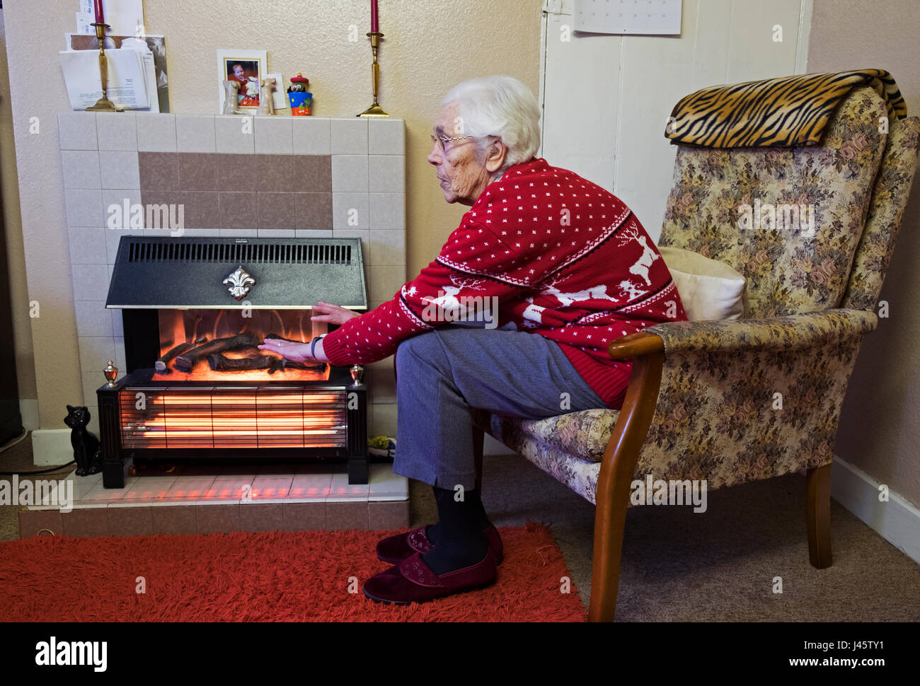 La vecchiaia pensionato riscaldando le mani accanto al fuoco elettrico Foto Stock