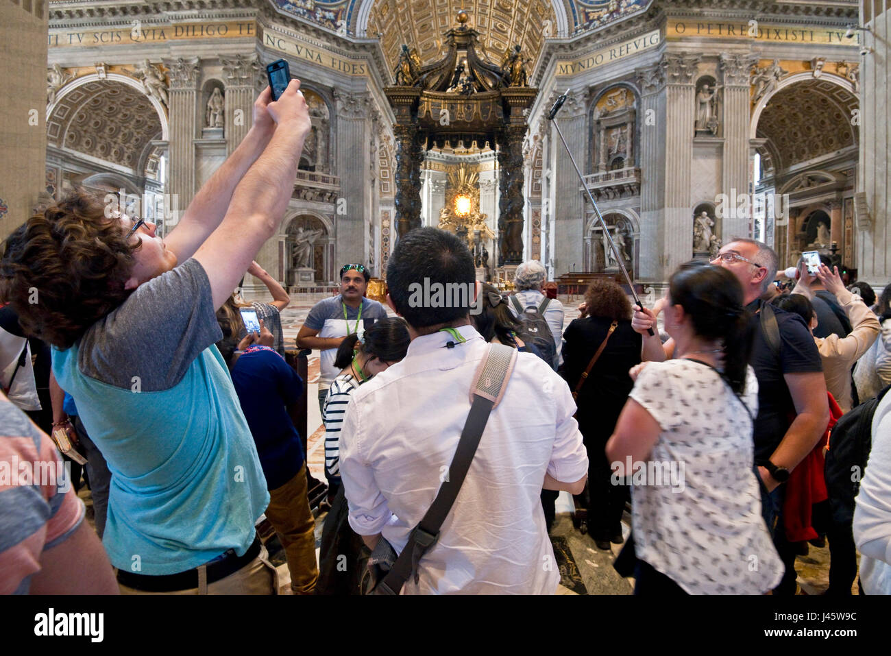 Un ampio angolo di vista interna all'interno della Basilica di San Pietro della principale alterare e la folla di turisti e visitatori tutti cercando di ottenere fotografie e selfies. Foto Stock