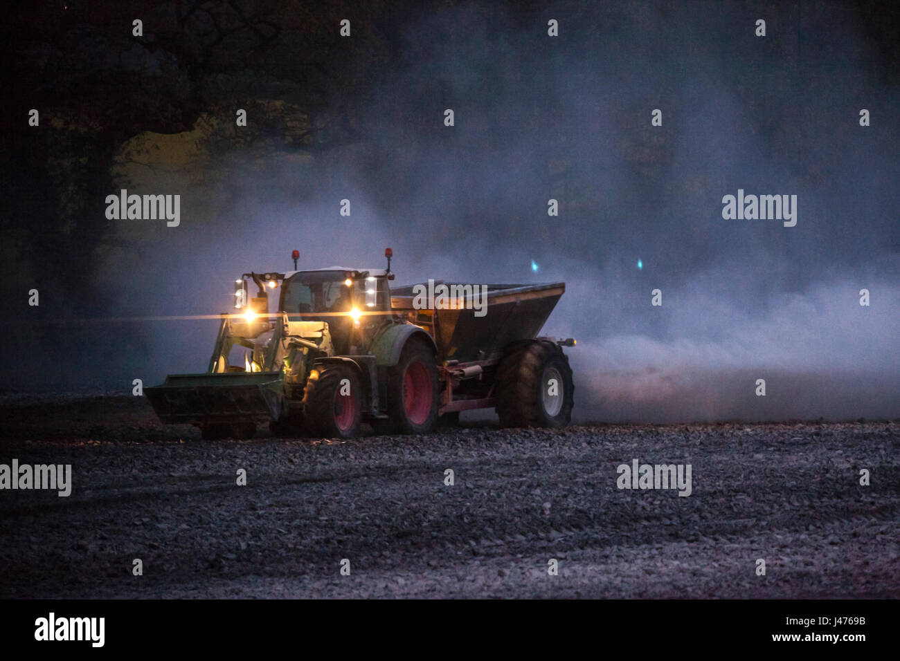 Imprenditore lavorare fino a tarda notte spandimento di calce dal suo le luci del trattore Foto Stock