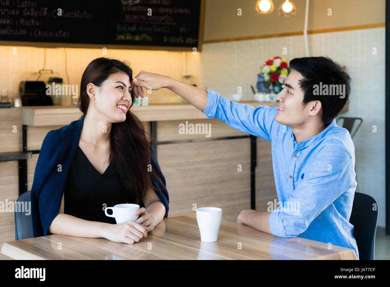 Asian bella donna sorridente quando i suoi capelli toccato dal suo fidanzato in cafe. Foto Stock