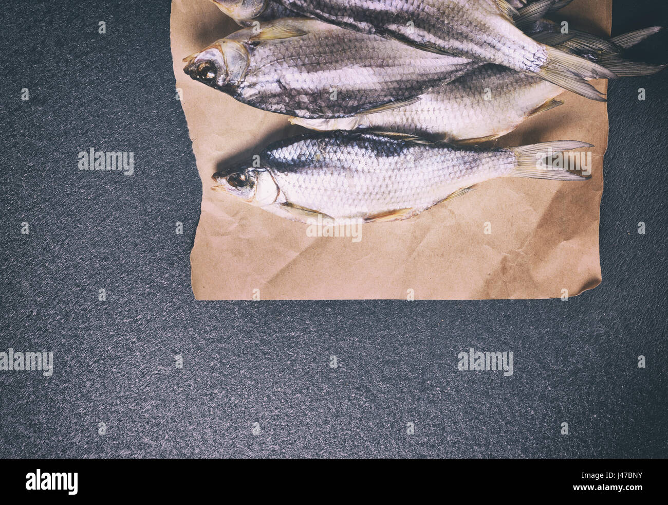 Tutto il pesce essiccati in roach bilance giacente su carta marrone, uno spazio vuoto al fondo tonificante vintage Foto Stock