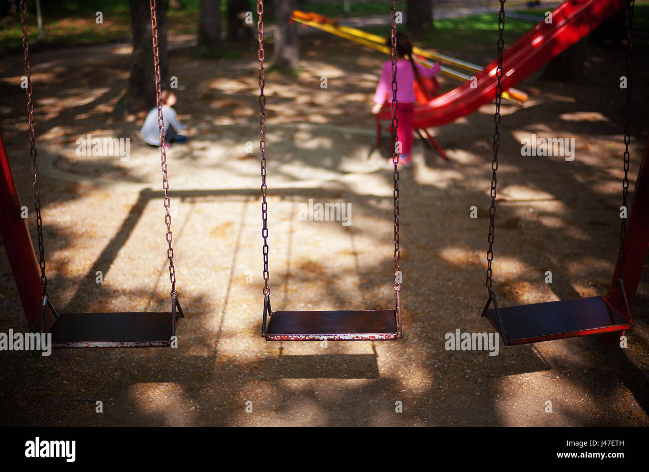 Dettagli del parco giochi nel parco della città, vista su tre altalene e due bambini in sfondo sfocato. Foto Stock