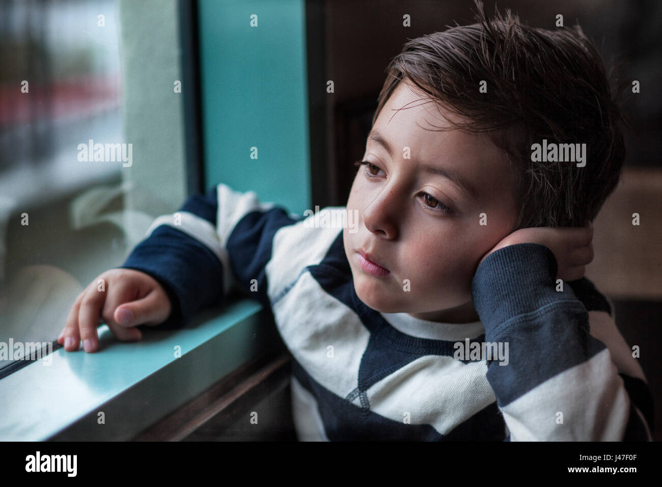 Ritratto di un sobrio little boy in blu e bianco spogliato della marina russa maglione staring al di fuori attraverso una finestra su un buio inverno mattina Foto Stock