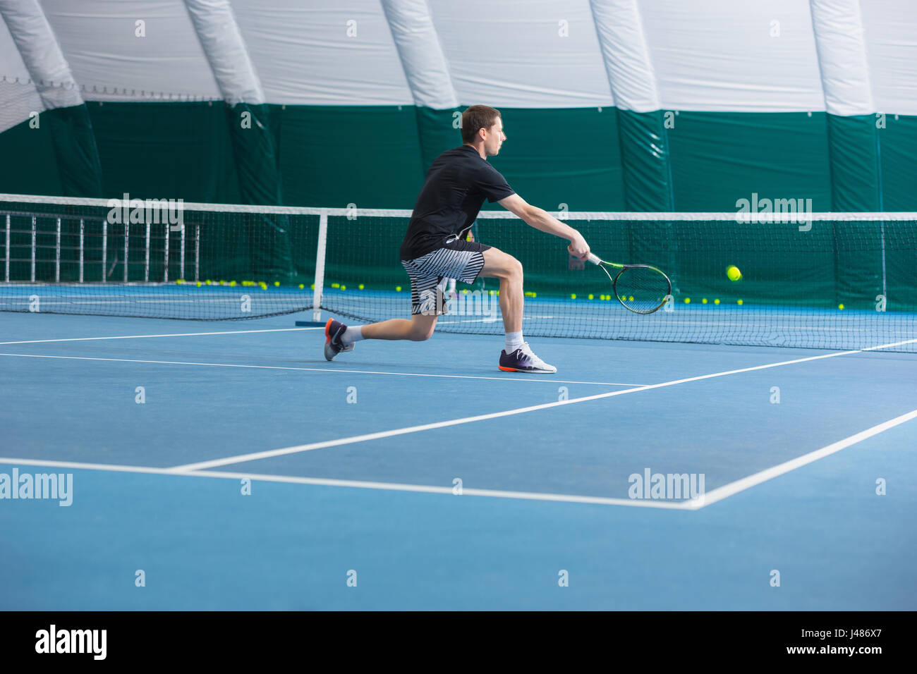 Il giovane uomo nel chiuso di un campo da tennis con sfera Foto Stock