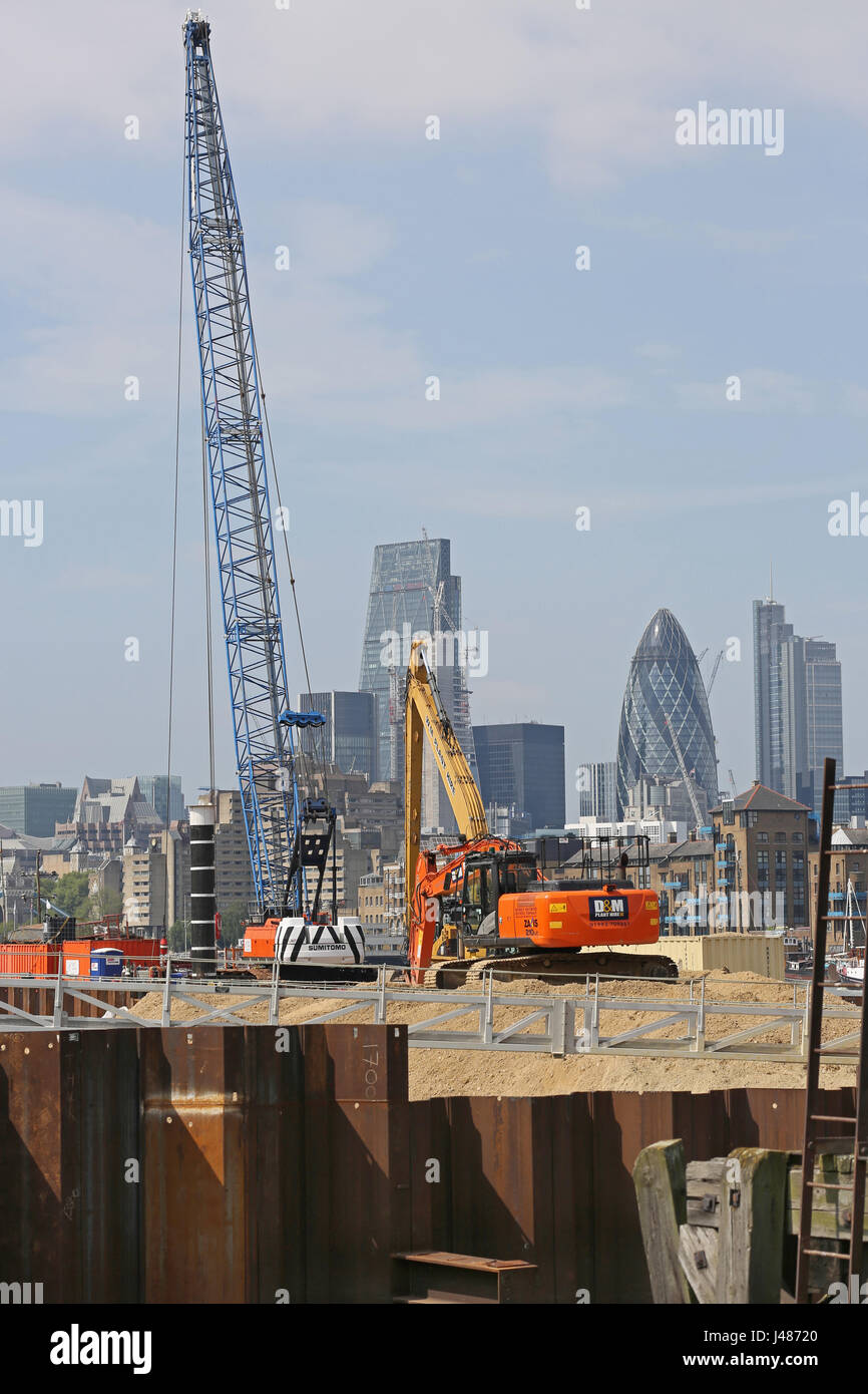 Thames Tideway progetto, Londra. Un escavatore e gru a cavalletto una temporanea paratoia a camere Wharf, Bermondsey. City of London skyline al di là. Foto Stock