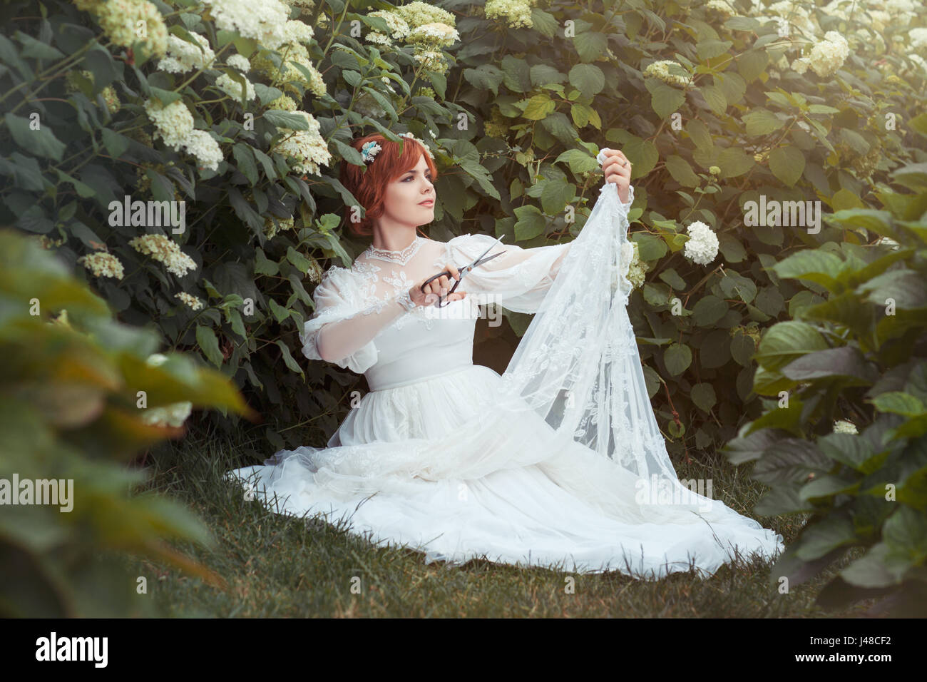 Tra gli arbusti da fiore ragazza con forbici fa un abito da sposa. Foto Stock