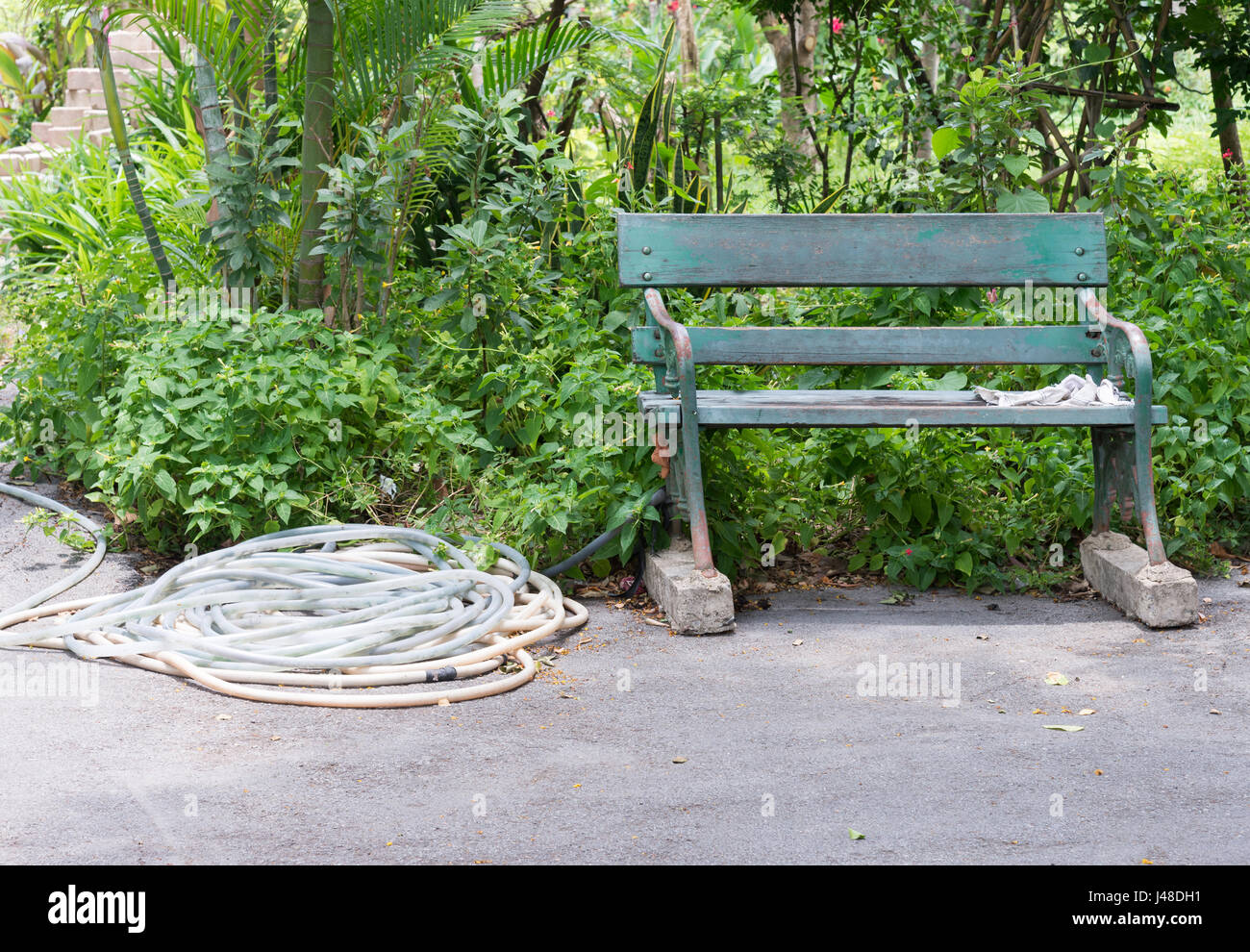 Il vecchio banco di metallo con il tubo di irrigazione in prossimità del percorso di cemento nel parco urbano. Foto Stock