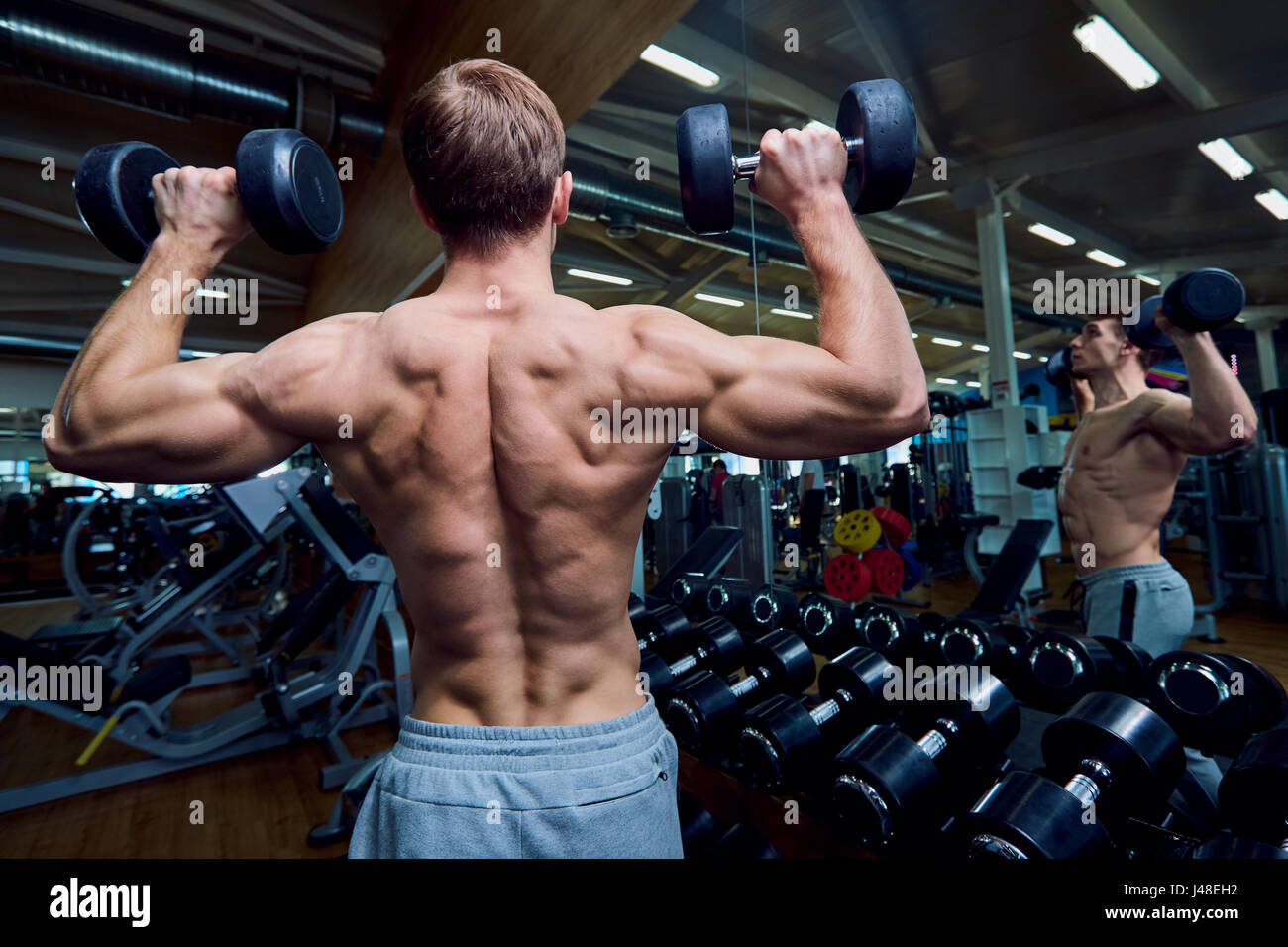 Vista posteriore di un uomo sportivo con manubri nelle sue braccia in palestra Foto Stock