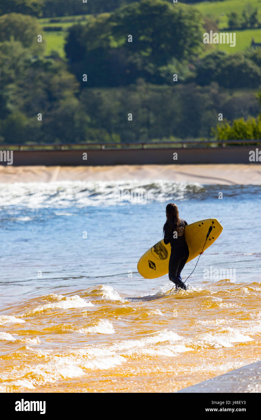 Un surfista holding tavole da surf a onde artificiali in piscina nel Conwy Valley sa come navigare Snowdonia, con l'alloggio glamping chalets Foto Stock